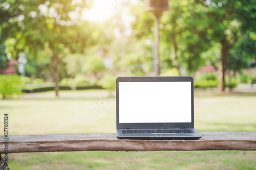A silver laptop with a blank screen. Placed on an outdoor wooden table for a park tree backdrop.