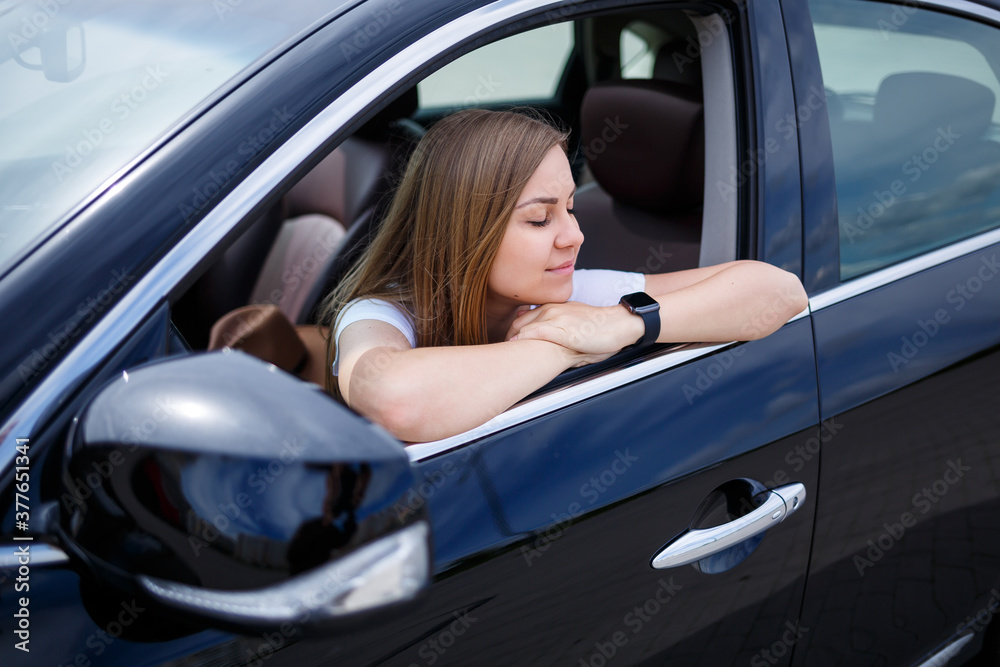 Young beautiful woman with long hair sits in a black car at a parking lot. Pretty girl in casual clothes. Car trip Young beautiful woman with long hair sits in a black car at a parking lot. Pretty girl in casual clothes. Car trip