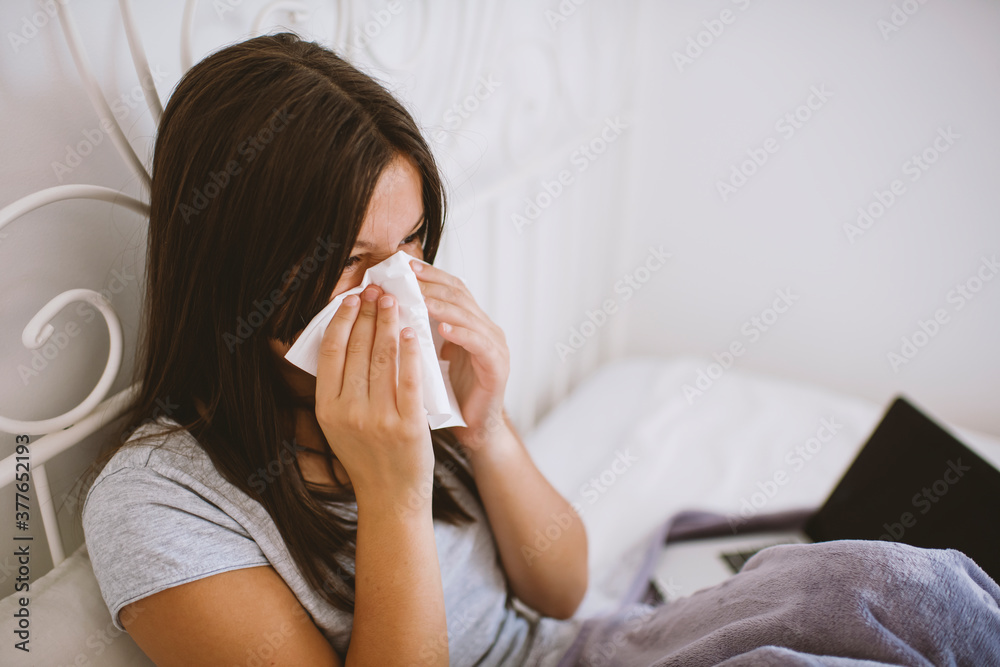 Ill Caucasian girl sneezing in napkin in white bed at home Ill Caucasian girl sneezing in napkin in white bed at home