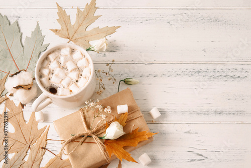 cocoa  ,hot chocolate with marshmallows, autumn yellow maple leaves,   gift box, a sprig of white flowers and cotton on a white wooden background