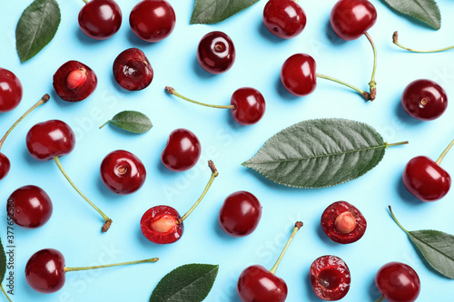 Fotografija Sweet juicy cherries with leaves on light blue background, flat lay