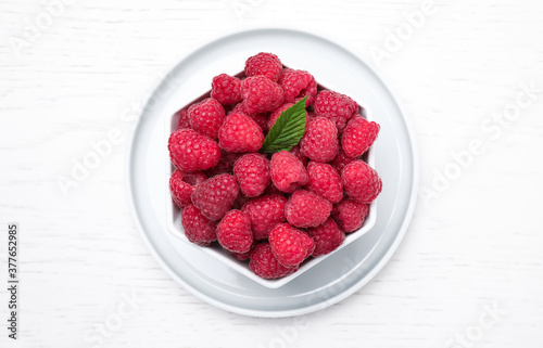 Delicious fresh ripe raspberries in bowl on white wooden table, top view