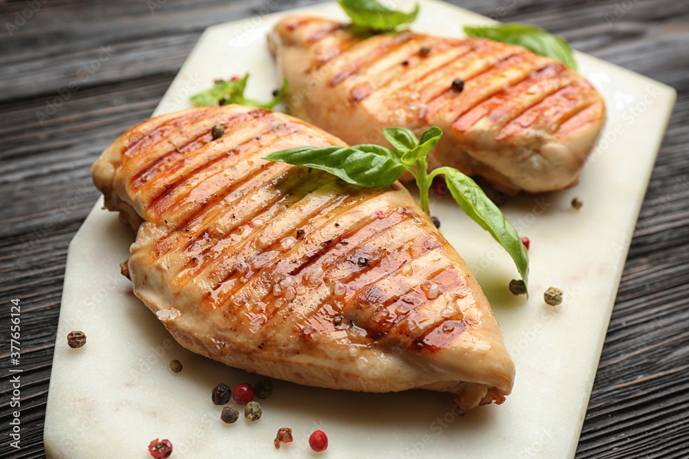 Tasty grilled chicken fillets with peppercorns and green basil on white marble board, closeup Tasty grilled chicken fillets with peppercorns and green basil on white marble board, closeup