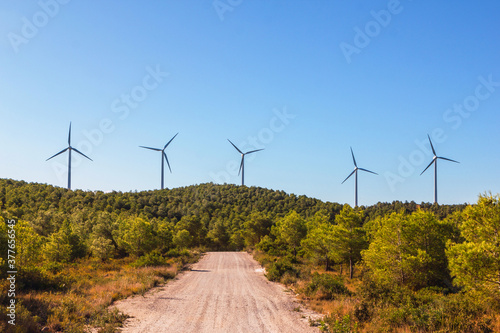 Stock photo of a windmills of a wind farm surrounded by trees and a mountain path