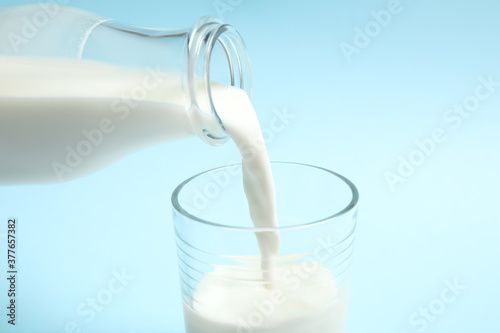 Pouring milk into glass on light blue background, closeup