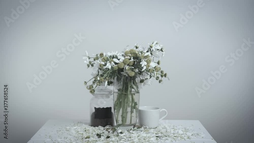 Bouquet of beautiful daisies stands in glass vase on dining table, showing the withering of life, white background. Acceleration of flow of time on example of flowers.