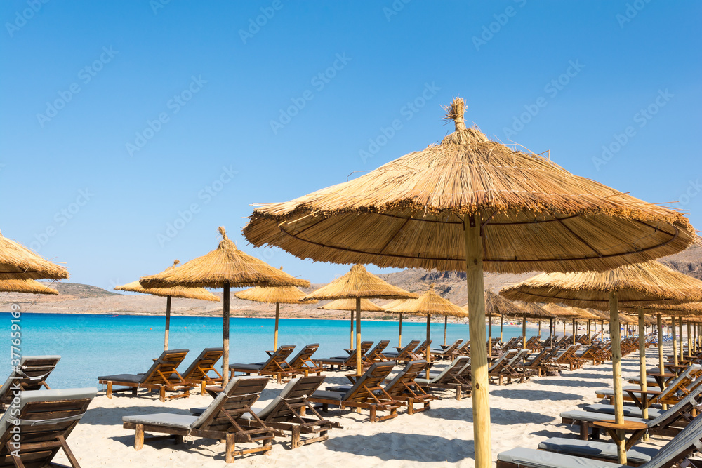 Straw umbrellas and wooden chaise longues on the beach
