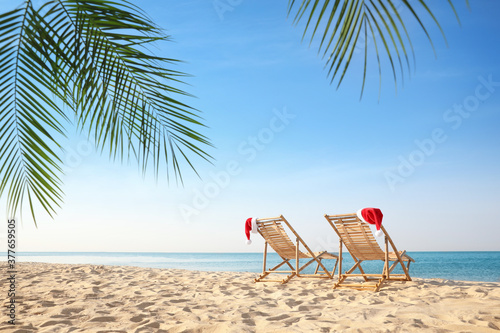 Sun loungers with Santa's hats on beach, space for text. Christmas vacation