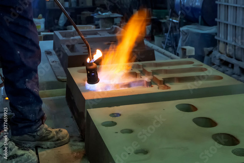 The worker is preheating to mold for casting. Sand casting, also known as sand molded casting, is a metal casting process characterized by using sand as the mold material.