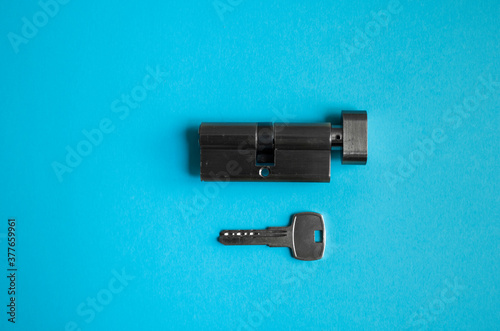A door lock cylinder core with key on the blue background. The cylinder of the lock with key. Installing a new lock on the door. Spare parts for the door.