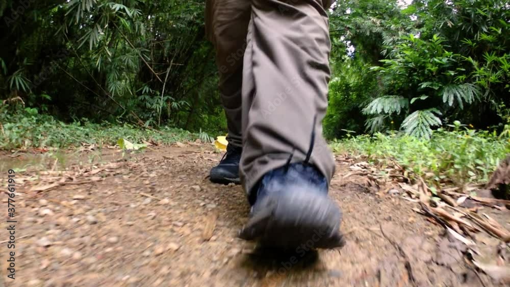 A man walking in the jungle, camera focused on his legs, showing him stepping forward on the dirt road with his shoes framed. A man walking in the jungle, camera focused on his legs, showing him stepping forward on the dirt road with his shoes framed.