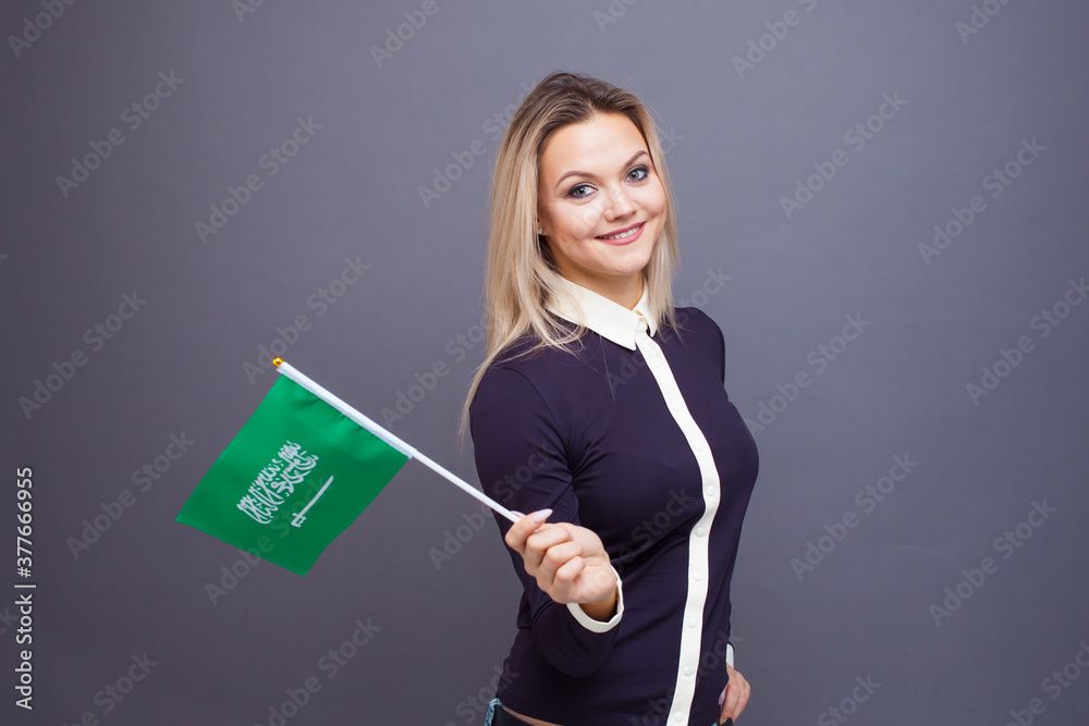 Immigration and the study of foreign languages, concept. A young smiling woman with a Saudi Arabia flag in her hand. Immigration and the study of foreign languages, concept. A young smiling woman with a Saudi Arabia flag in her hand.