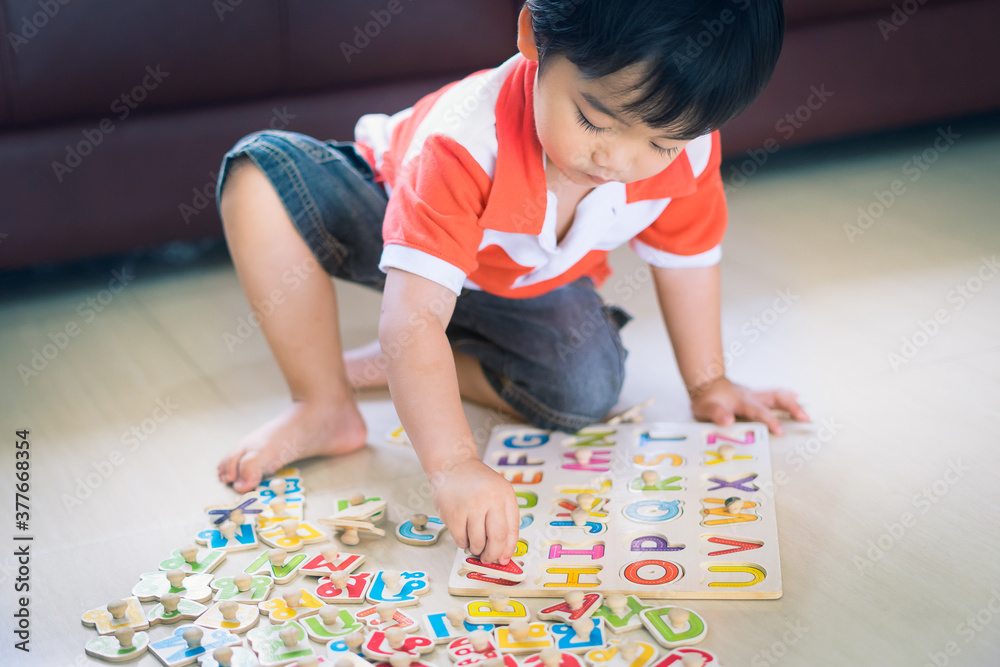 Asian little boy playing with wooden letter puzzle sitting on the floor at home, early education and leaning. Asian little boy playing with wooden letter puzzle sitting on the floor at home, early education and leaning.