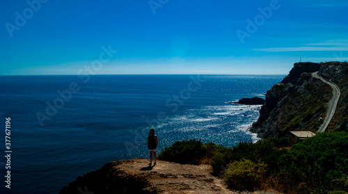 A woman looks at the horizon from a cliff.
