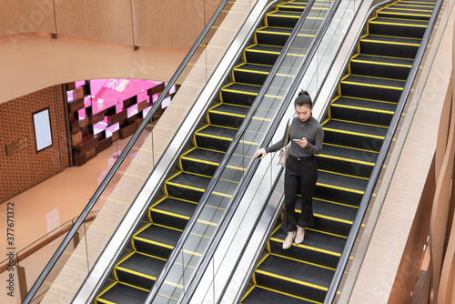Young lady using mobile phone on escalator