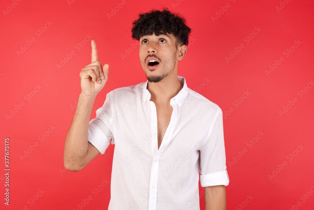 Young arab man with afro hair wearing shirt standing over isolated red background pointing finger up with successful idea. Exited and happy. Number one. Young arab man with afro hair wearing shirt standing over isolated red background pointing finger up with successful idea. Exited and happy. Number one.