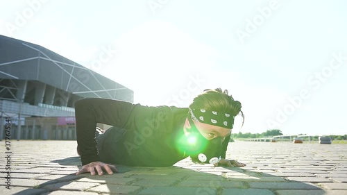 Front view of confident concentrated active young bearded man in mask dressed in black sportswear which doing push-ups on modern stadium photo