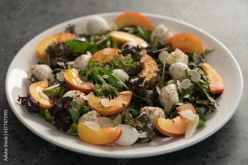 Closeup salad with nectarines, mozzarella and mixed greens in white plate on concrete background