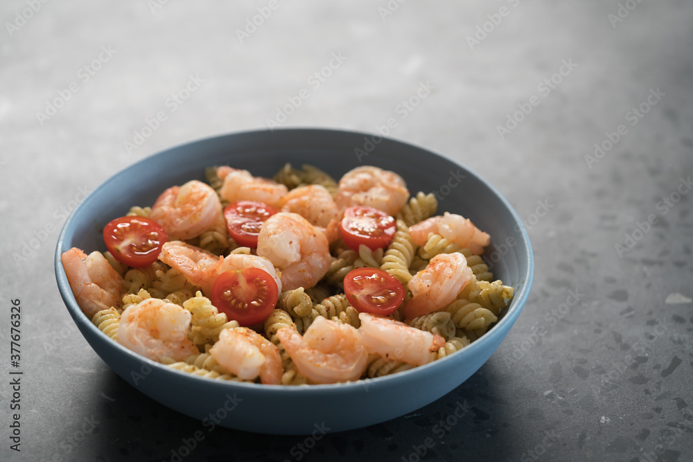 Fusilli with shrimps, cherry tomatoes and pesto in a blue bowl on concrete background Fusilli with shrimps, cherry tomatoes and pesto in a blue bowl on concrete background
