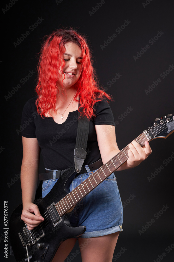 Obraz premium A teenage girl of the age of 12 years old plays an electric guitar while smiling on a black background