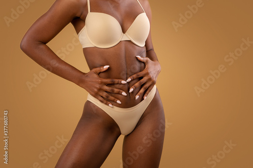 Fit Black Woman In Underwear Touching Belly While Posing Over Brown Background