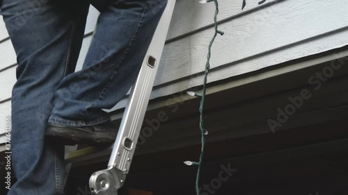man using a ladder to set up christmas lights