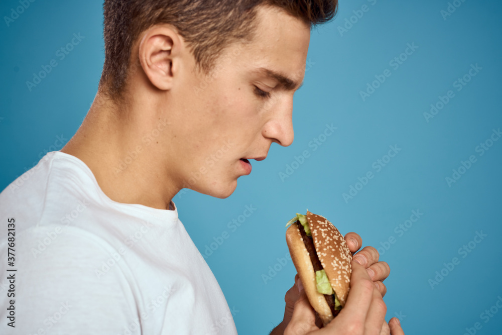 man with hamburger and white t-shirt blue background emotions gesturing with hands Copy Space man with hamburger and white t-shirt blue background emotions gesturing with hands Copy Space