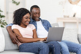 Joyful black man and woman watching photos on laptop