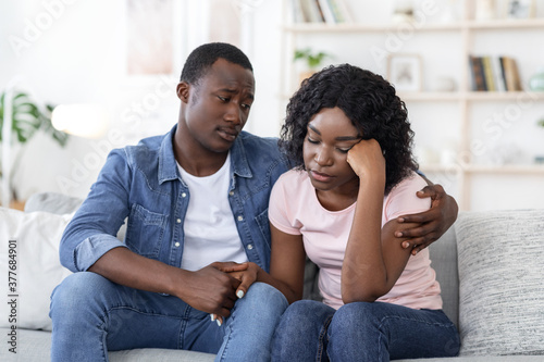 African husband comforting his crying woman, home interior