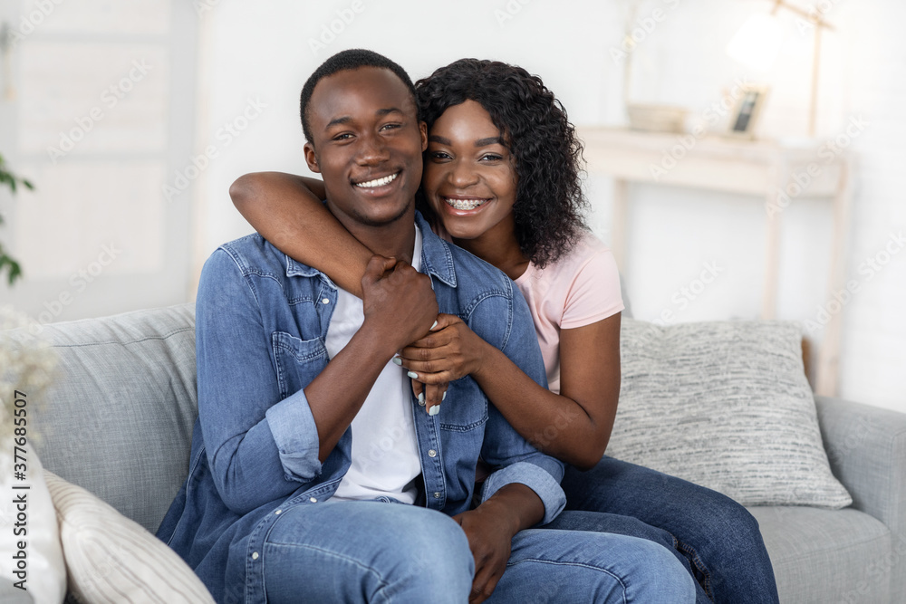 Loving black man and woman posing on couch at home