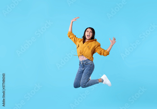 joyful young asian woman in yellow shirt jumping and celebrating over blue background.