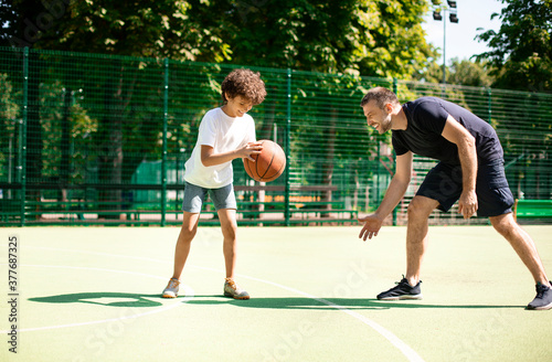 Mature coach teaching boy how to play basketball