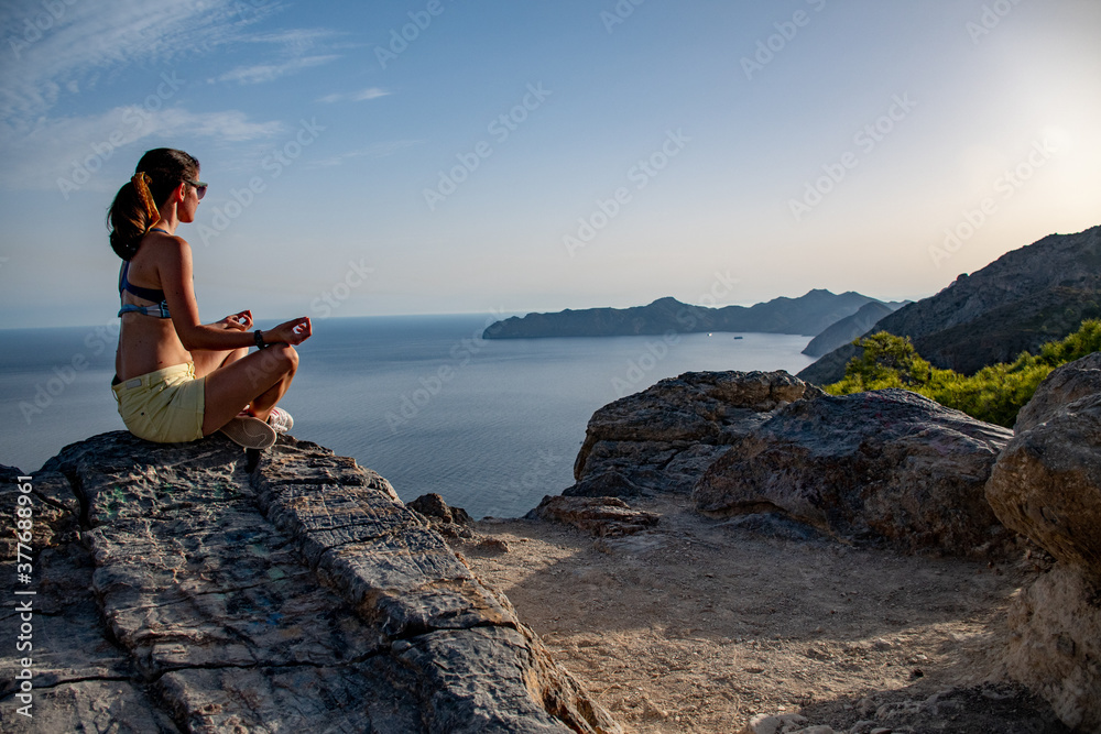 A beautiful woman doing meditation on a mountain with sea view