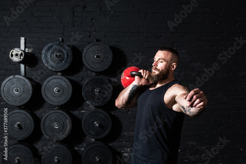 Young sweaty strong muscular fit man with big muscles doing hardcore cross kettlebell snatch workout training in the gym