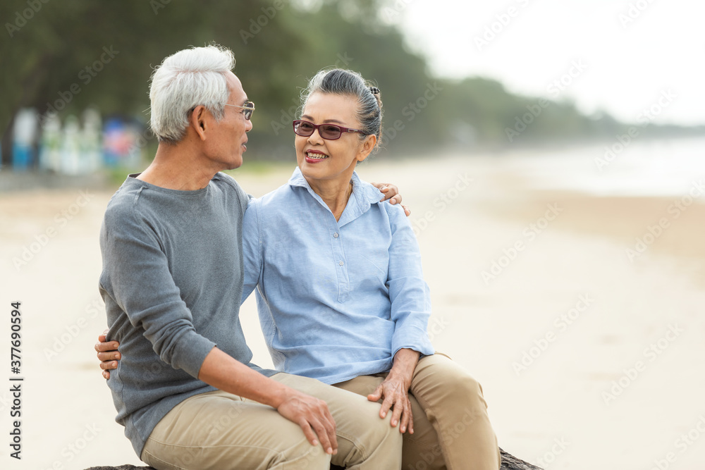 Fototapeta premium Asian Lifestyle elderly couple romantic lover hug and sitting on the beach happy in love romantic and relax time. Tourism older family travel leisure