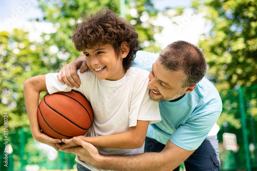 Joyful dad playing basketball with his son outdoors
