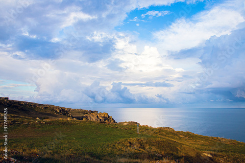 A beautiful view of the rocky coast, the sea coast with steep cliffs, paths among the tanned green grass, the blue sky with dark clouds, the blue sea on a morning autumn day.