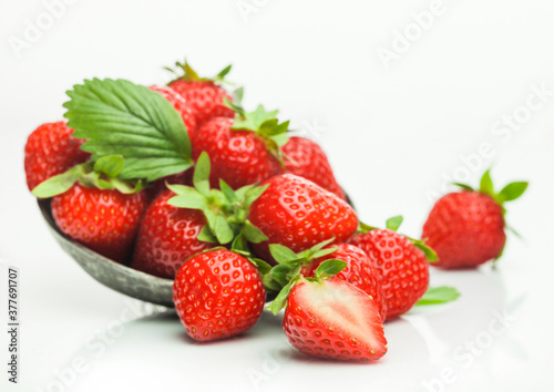 Fresh raw organic strawberries with leaf in steel bowl plate on white background with berries next to it.