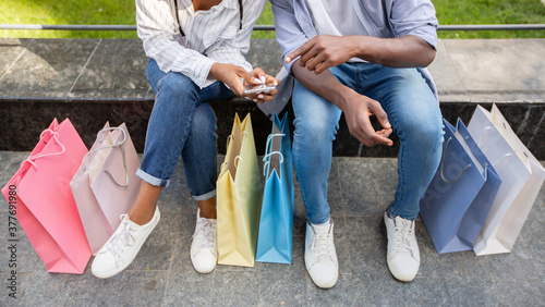 Share with followers emotions and photo of shopping. African american couple making photo of purchases in colorful bags