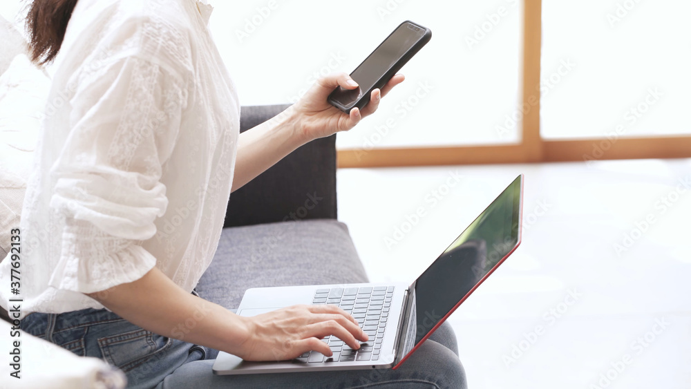 Naklejka premium ソファーでラップトップとスマートンを操作する若い女性