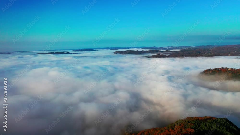 青い空と白い雲海の間から秋の山並みと城の覗く秋の夜明けの風景が美しい空撮風景