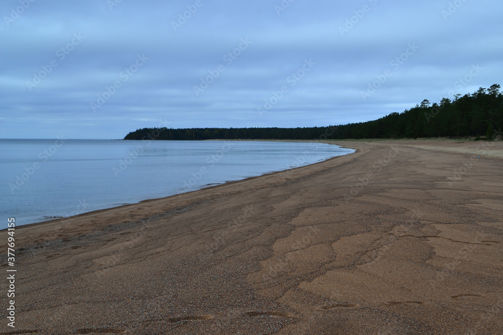 sandy shore of blue bay of Ladoga Lake in autumn, with trees on the horizon