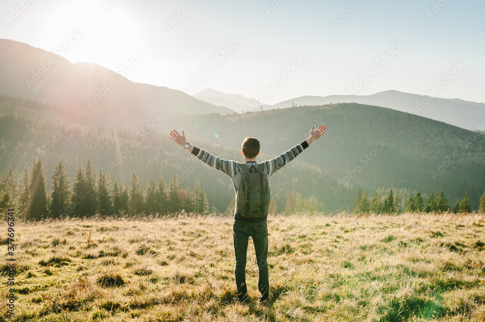 Happy man with backpack on sunset in autumn day with open hands. Back view. Hipster enjoying sunrise on peak mountains. Tourist traveler on background valley. Hiker looking sunlight in country Europa. Happy man with backpack on sunset in autumn day with open hands. Back view. Hipster enjoying sunrise on peak mountains. Tourist traveler on background valley. Hiker looking sunlight in country Europa.