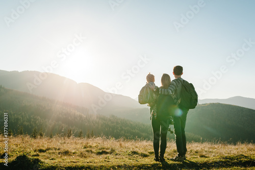 The daughter hug parents on nature. Mom, dad, and child walk in the grass. Family spending time together in mountain outside, on vacation. Family holiday trip concept. World Tourism Day. Back view.