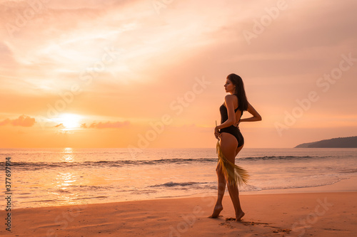 Young woman in bikini standing in water and is splashed by sea waves at sunset