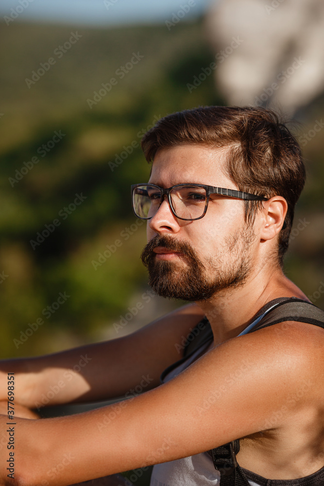 Young male hiker with backpack relaxing on top of a mountain during calm summer sunset Young male hiker with backpack relaxing on top of a mountain during calm summer sunset