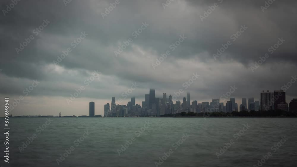 Panning up panoramic city skyline view timelapse of Chicago with dramatic storm clouds in the sky moving over the water of Lake Michigan at sunset as day turns to night and building lights turn on. Panning up panoramic city skyline view timelapse of Chicago with dramatic storm clouds in the sky moving over the water of Lake Michigan at sunset as day turns to night and building lights turn on.