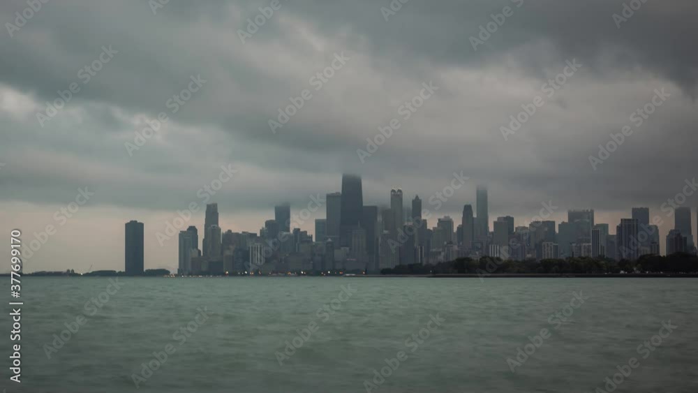 Panning out panoramic city skyline view time lapse of Chicago with dramatic storm clouds in the sky moving over the water of Lake Michigan at sunset as day turns to night and building lights turn on. Panning out panoramic city skyline view time lapse of Chicago with dramatic storm clouds in the sky moving over the water of Lake Michigan at sunset as day turns to night and building lights turn on.