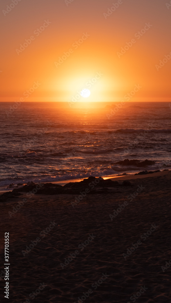 Bright orange sun on horizon over ocean. Summer afternoon on beach in Portugal. Vertical aspect ratio.