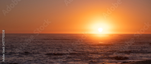 Bright vivid sun on horizon over ocean at sunset  with reflections on water. Wide aspect ration with copy space on left.